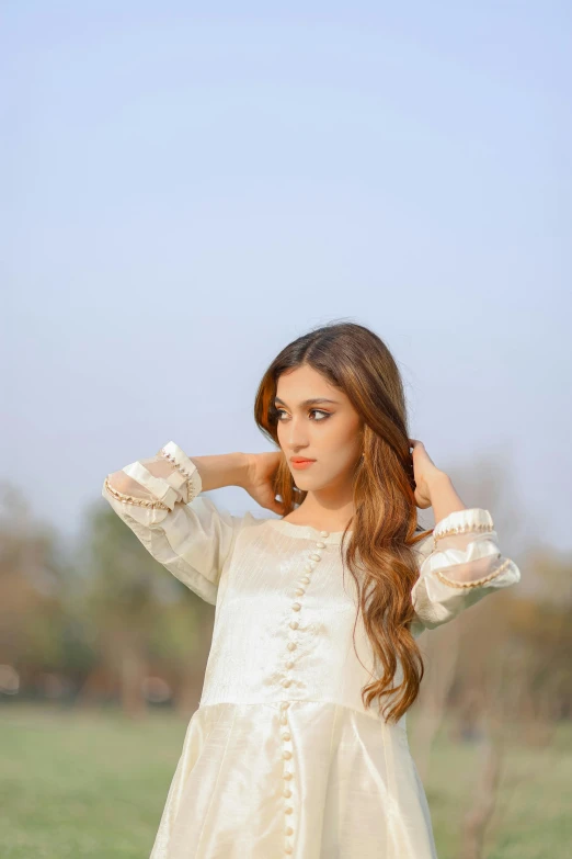  with long wavy hair wearing white dress standing in grassy field