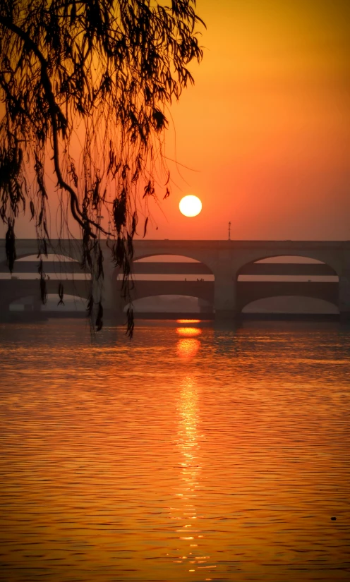 a bright sun sets over the water from a bridge