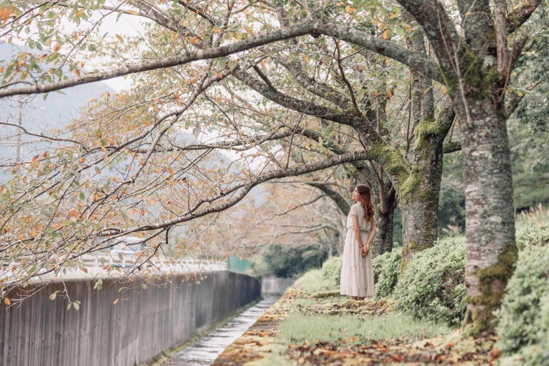 a young lady standing next to trees with leaves