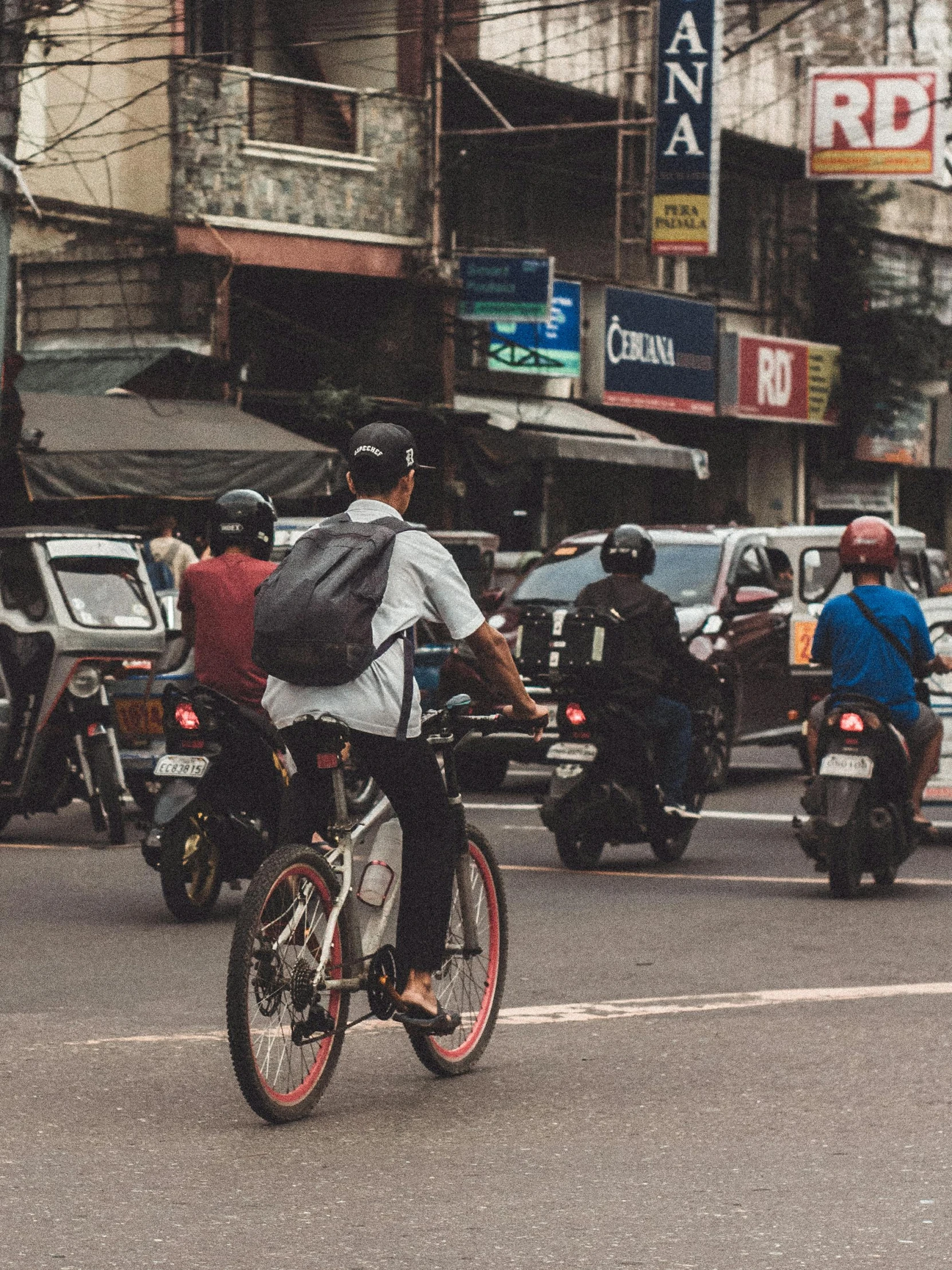 motorcyclists on an urban street with many parked cars