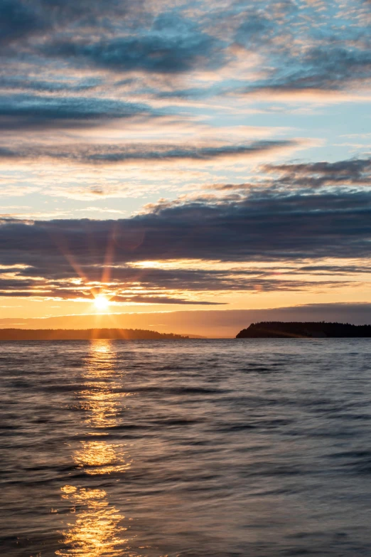 the sunset on a calm lake with a large island in the distance