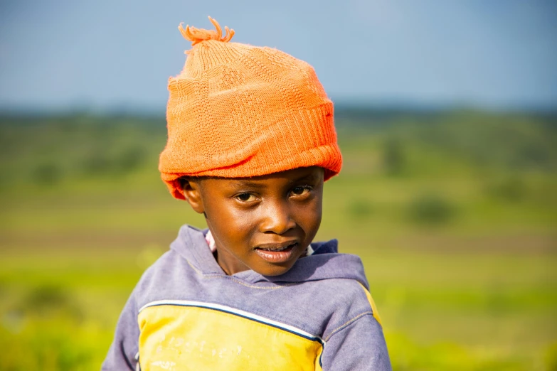 a little boy wearing an orange hat looking at the camera