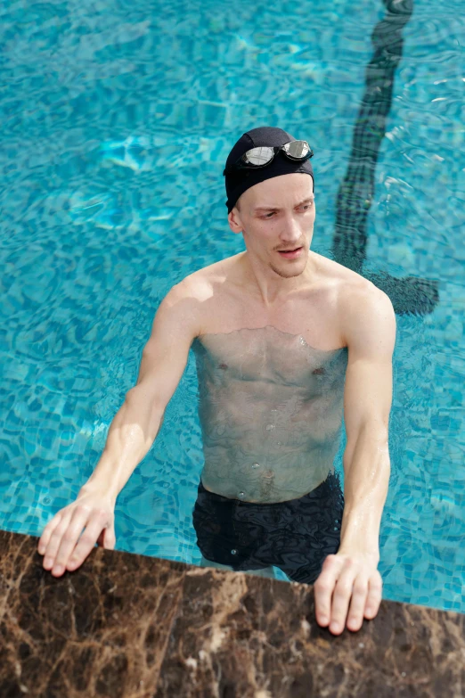 a man in swimming trunks next to an aqua pool