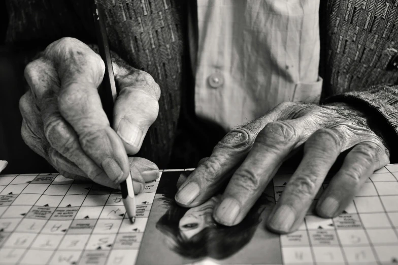 man with wrinkled hands sitting at a table and playing board game