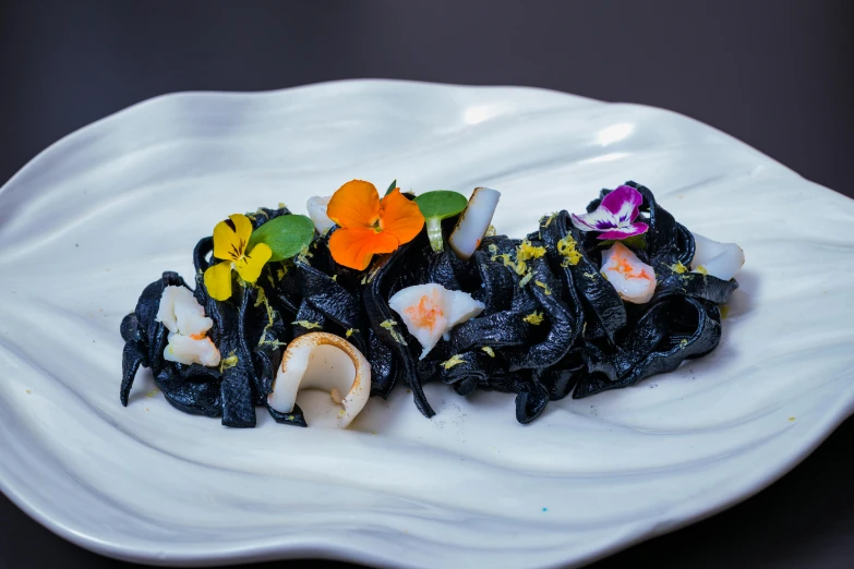 a dish with black pasta and flowers on it