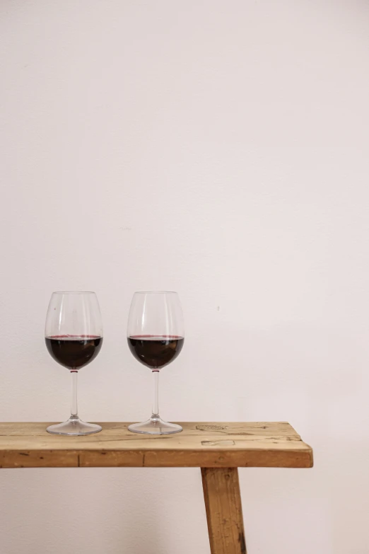 two wine glasses filled with red wine on top of a wooden table