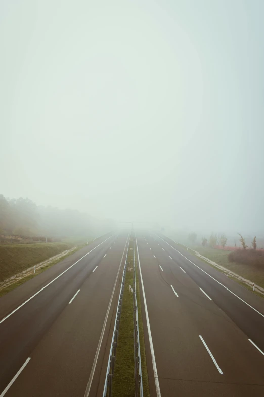 an empty highway surrounded by green grass and trees