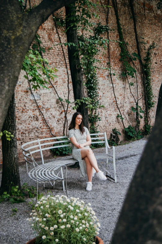 a woman sitting on top of a metal chair next to a tree