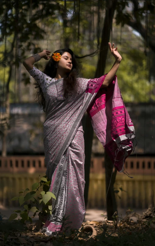 a woman is posing by a tree while dressed in a pink sari