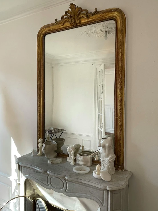 a very ornate mirror and some white vases on a mantle