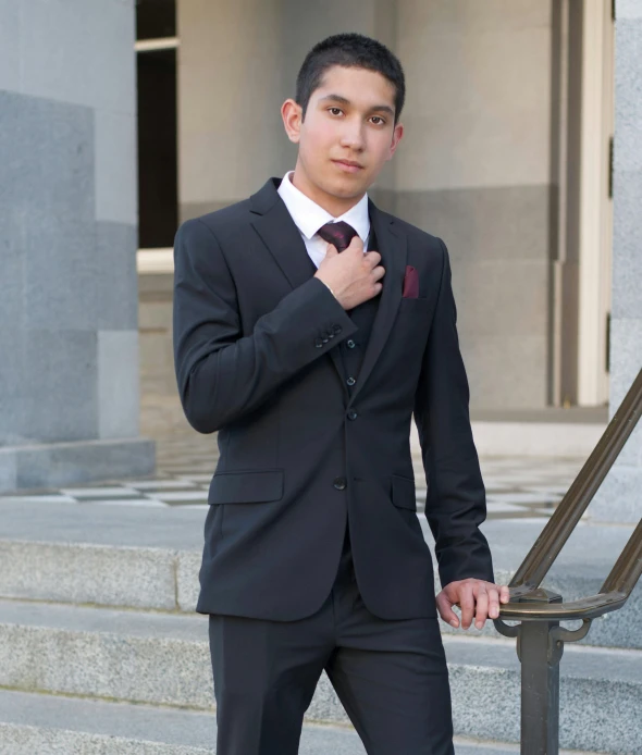 young man in suit and tie, holding onto his collar