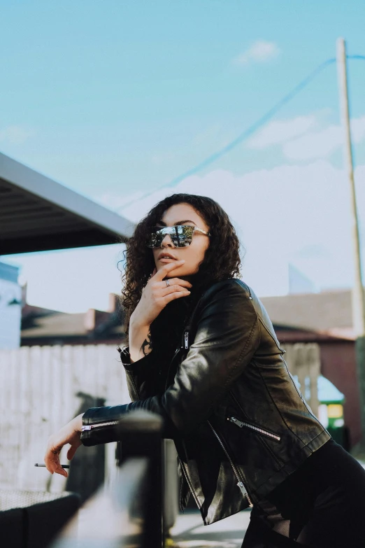 a woman wearing glasses leaning against a fence