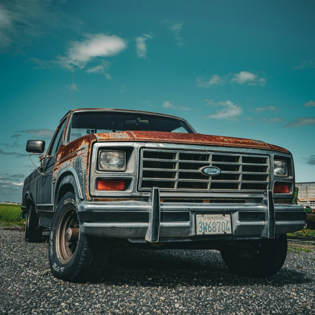 an old ford truck sits parked on a gravel parking lot