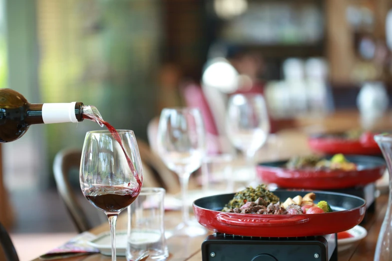 someone pours red wine into a glass in a restaurant setting