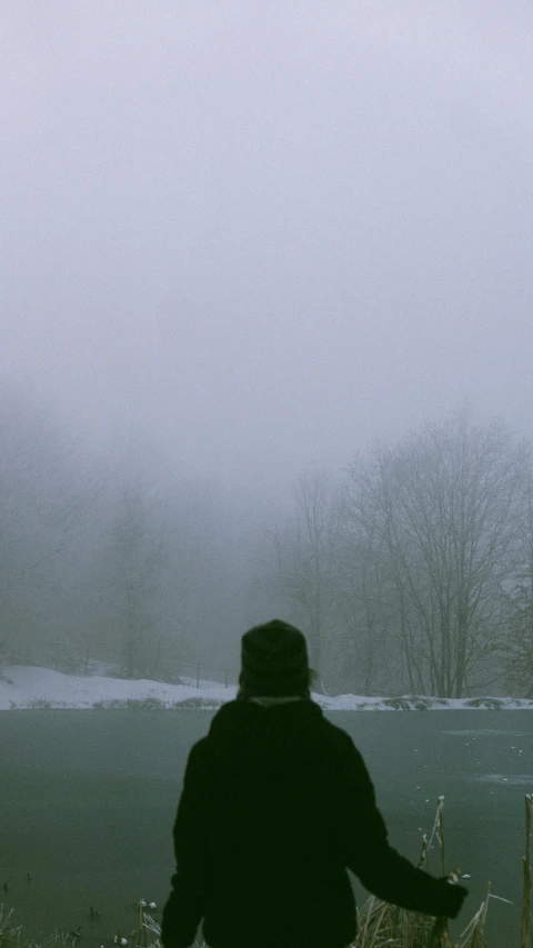 man is standing in front of water during a foggy day