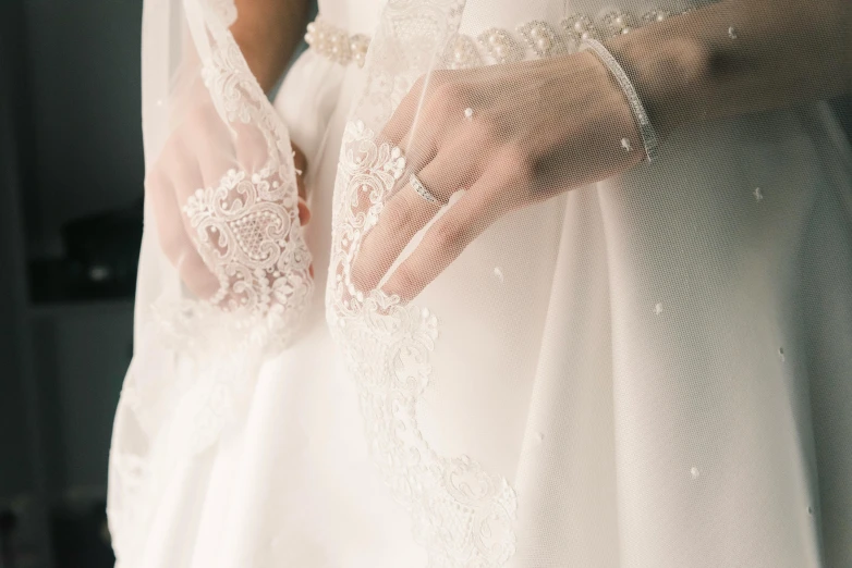 two brides hands wrapped in veils by wedding rings