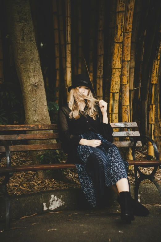 a blonde woman in black jacket sitting on a bench near bamboo trees