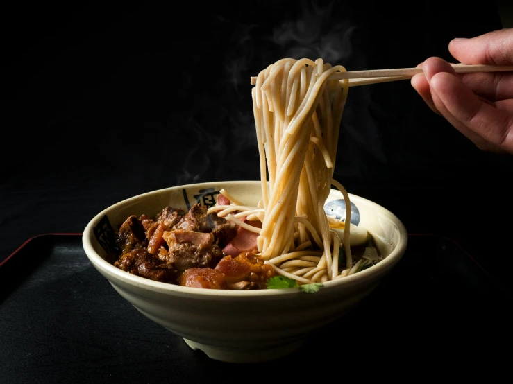 a bowl with noodle and meat in it being held by chopsticks