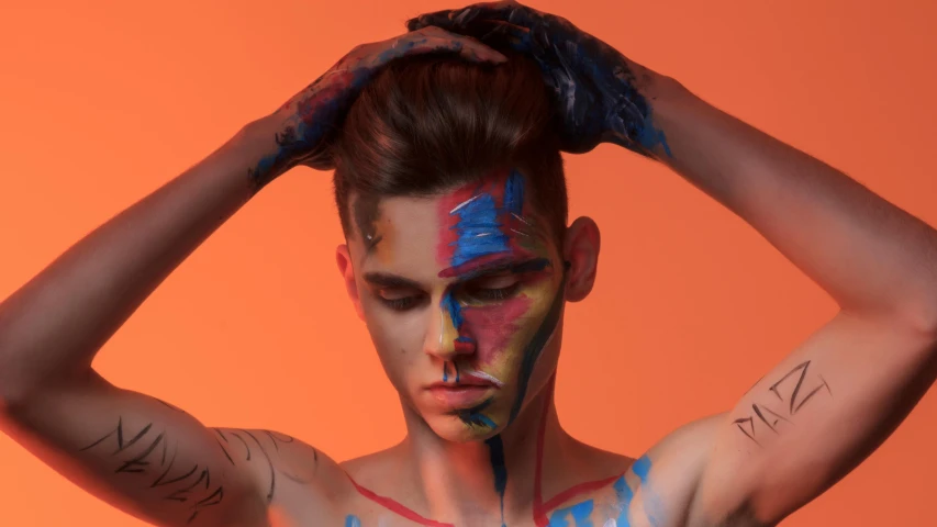 man with face painted with different colors on orange background