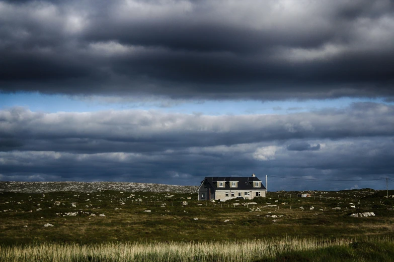 house in an open field with storm clouds in the sky