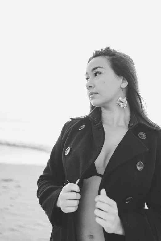 woman with jacket on standing on beach by water