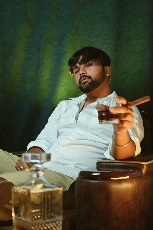 man sitting on a chair holding glass while smoking