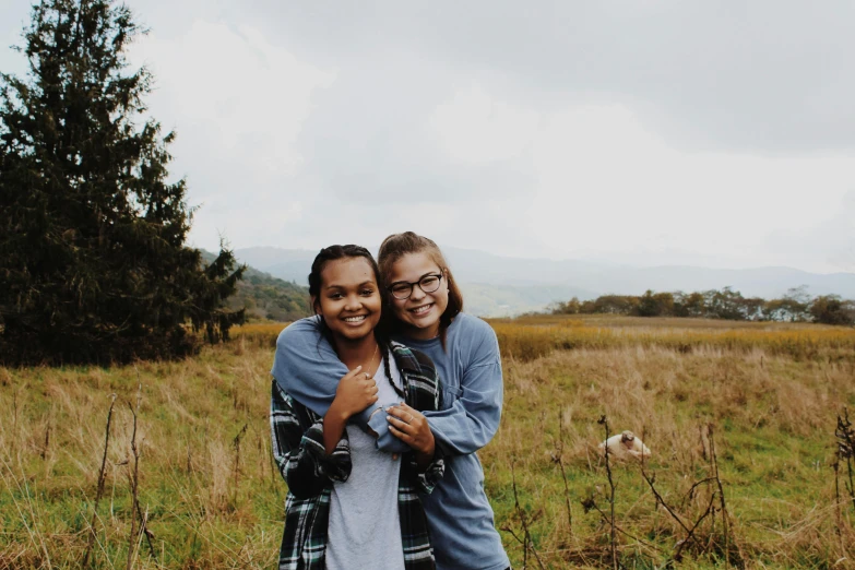 two girls are smiling and hugging in the field