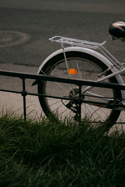 a bicycle parked by a metal fence in some grass