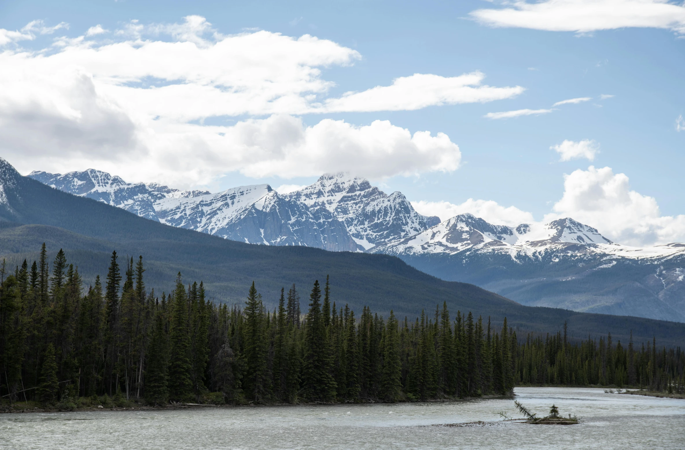 a group of mountains covered in snow with a river running beside