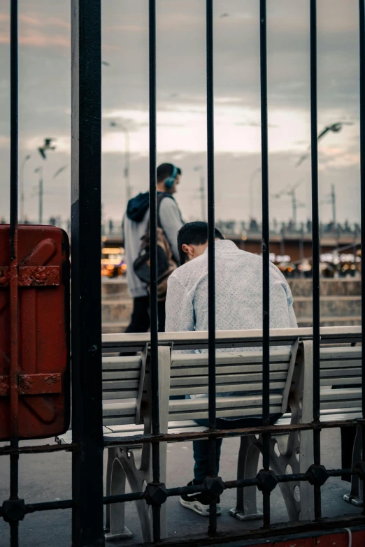 two people sitting on the edge of a park bench, one person sitting in the middle of the bench