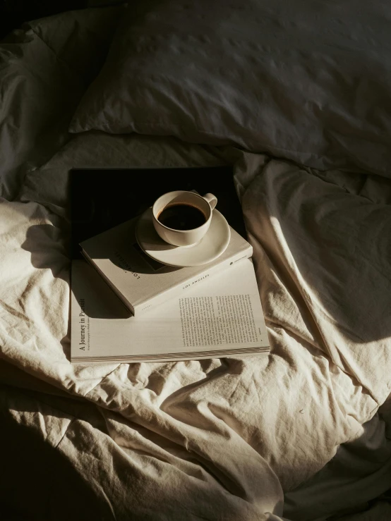 an open book and a mug are sitting on an unmade bed