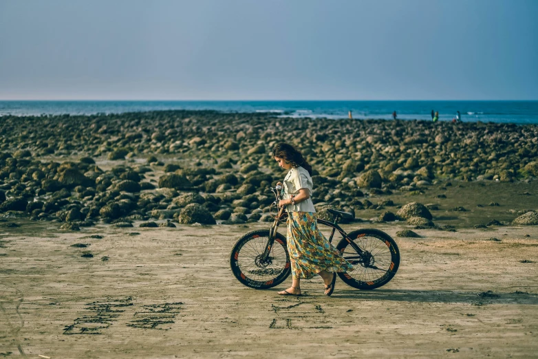 a woman walking her bike down the beach