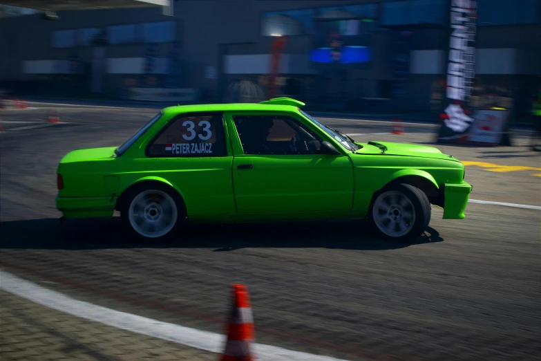 a green sports car driving in a lot next to buildings