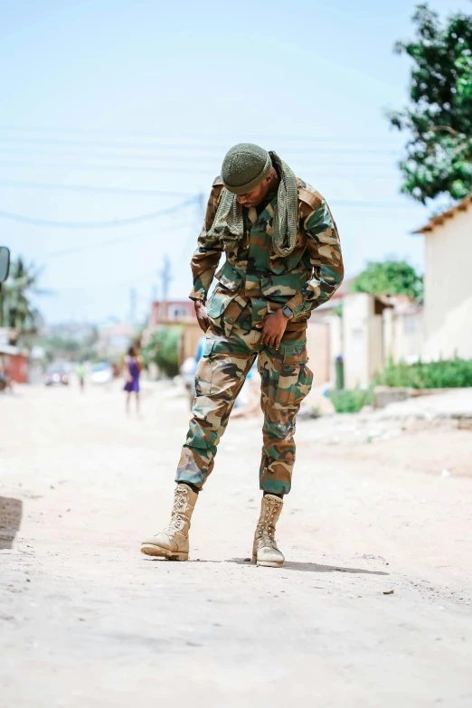 a soldier in camouflage standing and checking his shoes