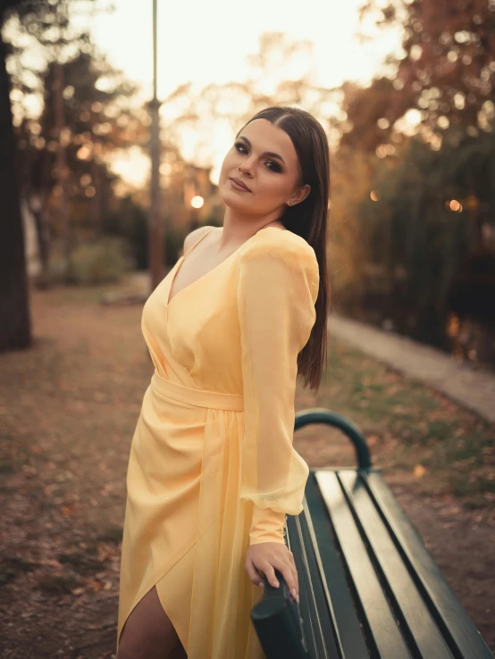 a woman wearing a yellow dress posing on a bench