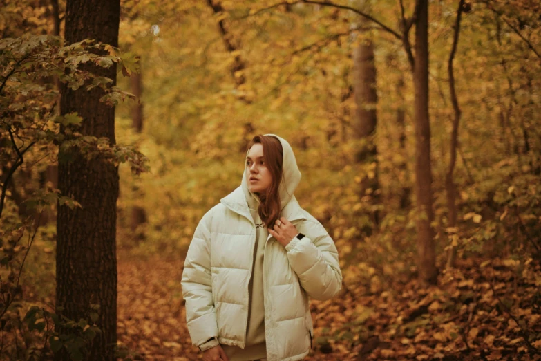 a woman in a coat and hood standing next to a tree