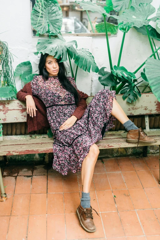 the woman is sitting on a bench near a plant