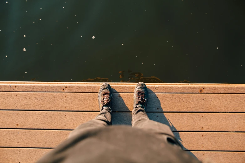 the view of a person's feet standing on a dock next to a lake