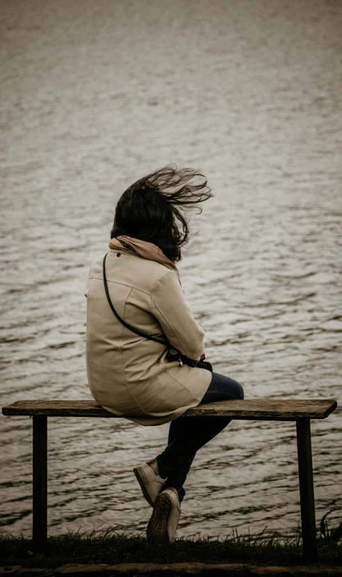 the girl is sitting on the bench by the lake