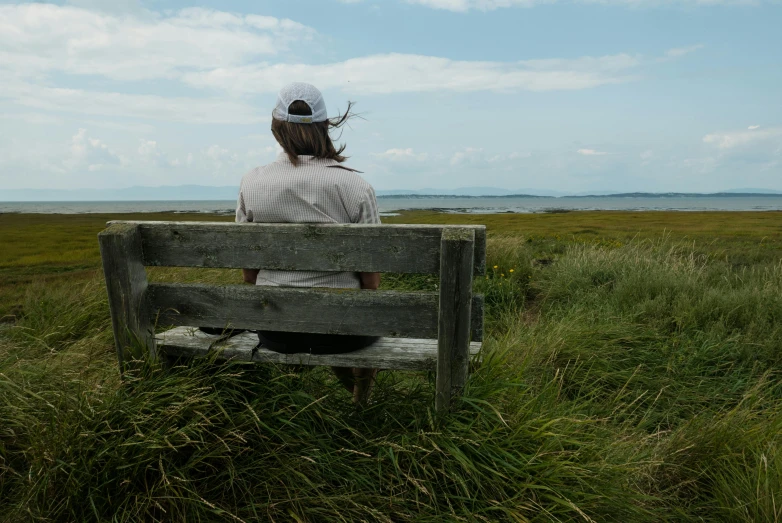 a person sits on a wooden bench overlooking a field and waterway