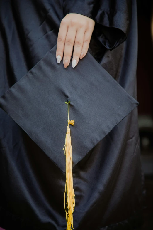 a female student wearing a graduation gown and with her hand holding a tassel
