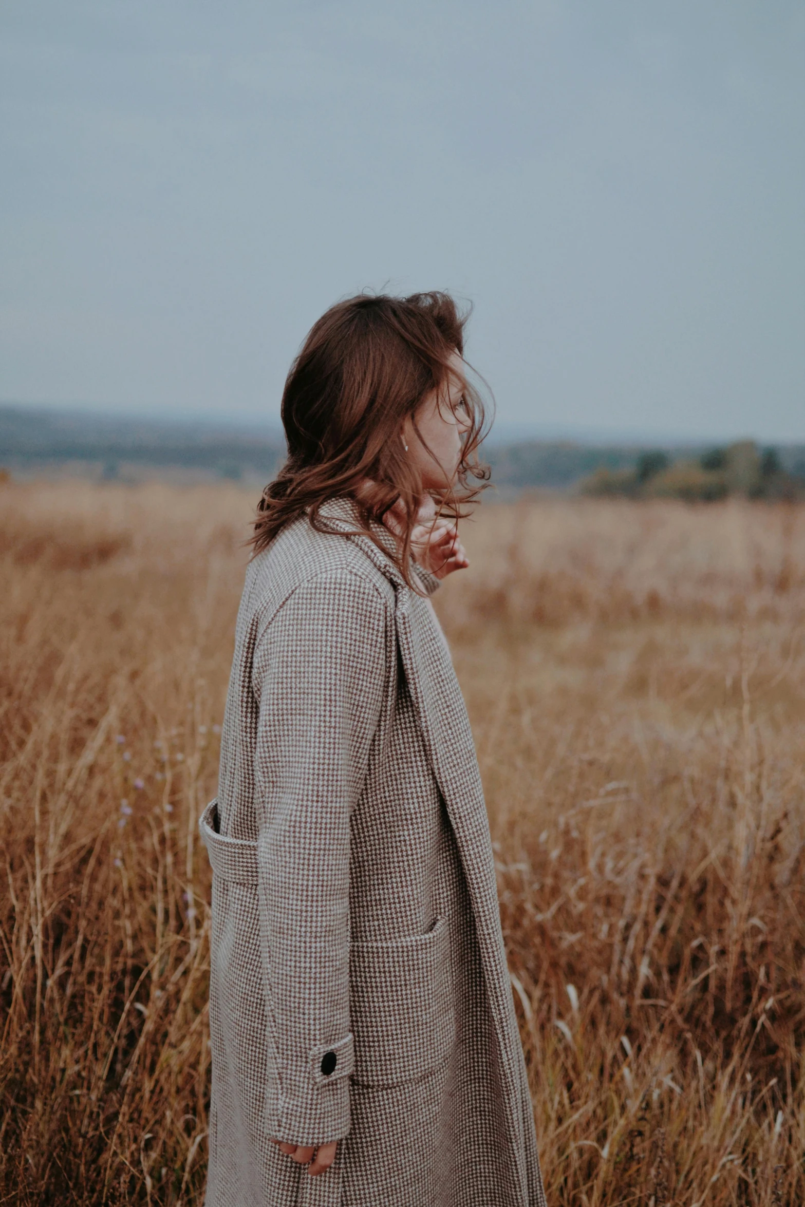 a woman standing in a field of tall grass, smoking a cigarette