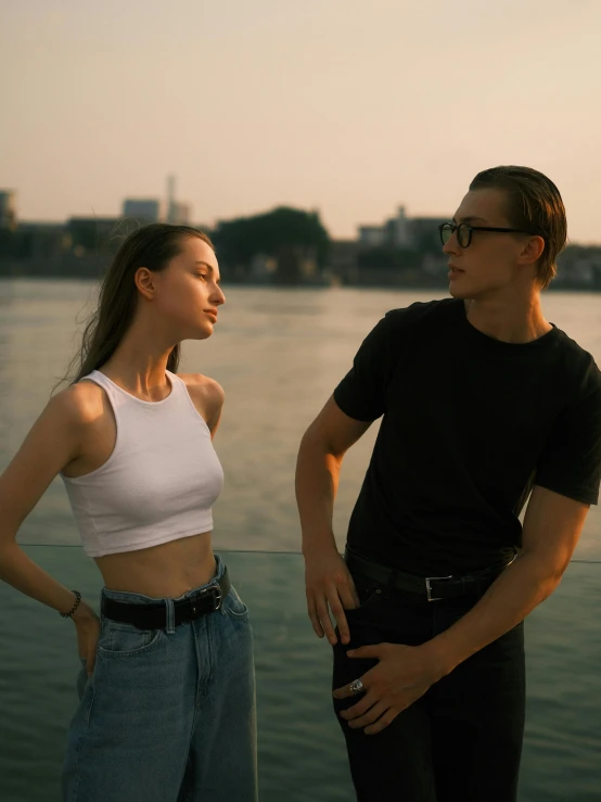 two people standing close to each other by the water