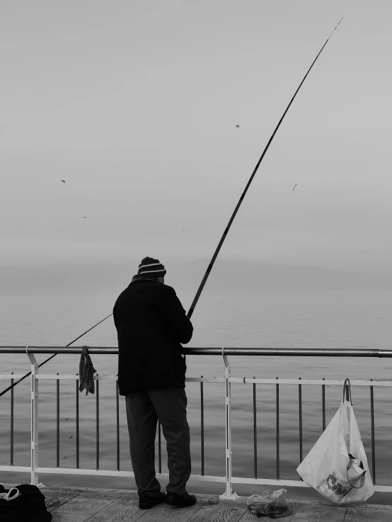 the man is fishing on the river by the fence