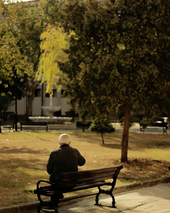 an older person is sitting on a bench outside