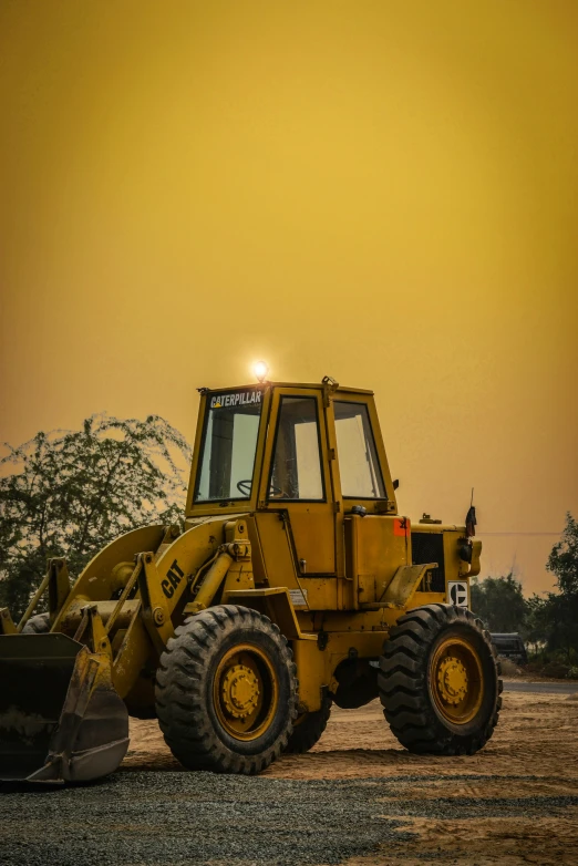 large yellow construction truck parked on gravel with trees in background