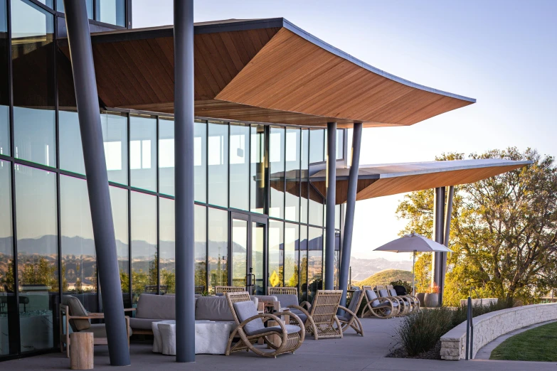 a glass building with chairs and an umbrella next to a lake