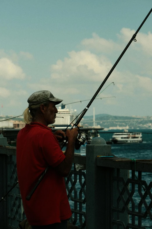 a man in red shirt fishing on pier by the ocean