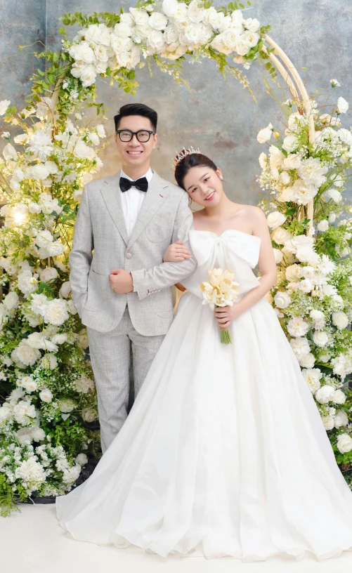 man and woman posing with white flower bouquet in front of a backdrop