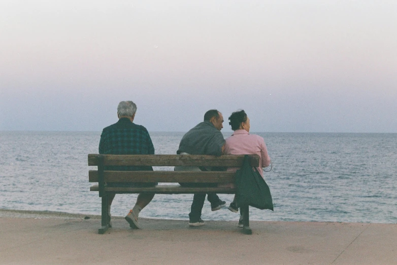two men and a woman sitting on a bench next to the beach